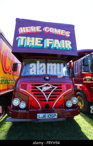 Southend on Sea, Royaume-Uni. 25 mars 2016. Un camion de foire Foden rouge classique avec des détails chromés et un panneau vibrant indiquant « HERE COMES THE FAIR », garé sur l'herbe à côté d'autres véhicules vintage showman. Le camion évoque la nostalgie des foires itinérantes britanniques traditionnelles et de la culture des showmen. Carter's Steam Fair est à Southend pour les vacances de Pâques. La célèbre foire amusante vintage avec une gamme de manèges magnifiquement restaurés. Penelope Barritt/Alamy Live News Banque D'Images