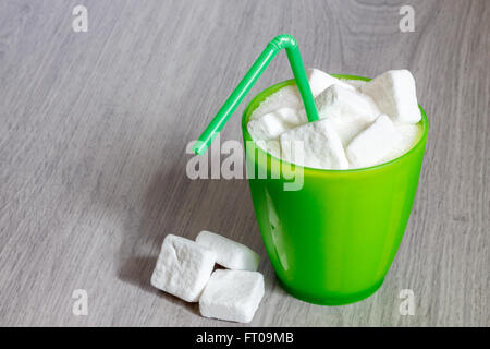 Verre en Plastique vert avec de la paille plein de sucre et de cubes de sucre. Image Concept pour trop de sucre dans les sodas, jus de fruits, boissons, soft Banque D'Images