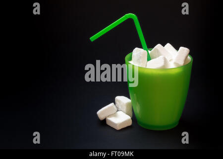 Verre en Plastique vert avec de la paille plein de sucre et des morceaux de sucre sur fond noir. Image Concept pour trop de sucre dans les sodas Banque D'Images