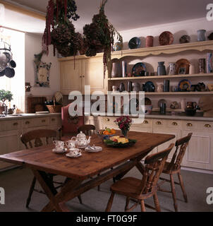 Old pine table et chaises en pays cuisine avec collection de poterie sur étagères crème vintage Banque D'Images