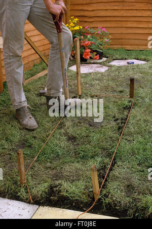 Close-up d'un jardinier creuser vers le haut avant la pose du gazon dans une pelouse de pavage Banque D'Images