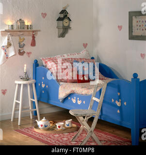 Coussins colorés vérifié sur peint en bleu lit dans la chambre de l'enfant avec une chaise en bois et selles Banque D'Images