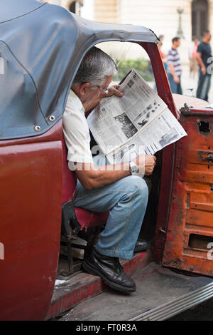 La vie quotidienne à Cuba Cuba - homme assis dans la vieille voiture avec porte ouverte journal de lecture à La Havane, Cuba Banque D'Images