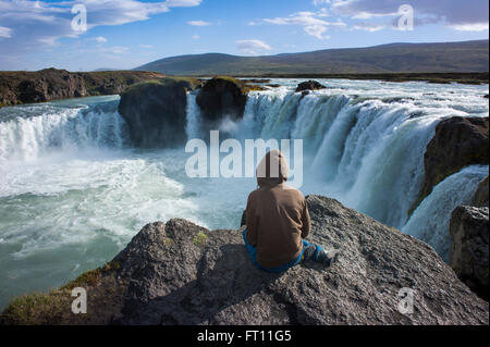 Femme assise sur un rocher au-dessus de la cascade Godafoss, Nordurland Eystra, Islande Banque D'Images