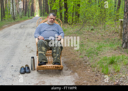 Senior man sleeping tandis que reste dans la forêt assis sur un rocking-chair en osier Banque D'Images