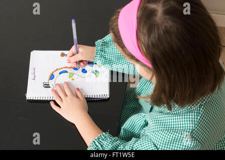 Petite fille avec un plaid vert smock dimensions un dinosaure dans un ordinateur portable à la maison Banque D'Images