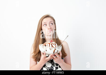 Les expressions du visage humoristique d'une jeune femme alors qu'elle considère l'énorme coupe de glaces qu'elle détient. Banque D'Images