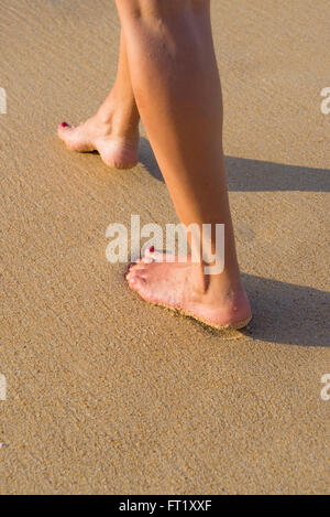 Voyages Plage - femme marchant sur la plage de sable en laissant des traces de pas dans le sable. Closeup détail des pieds féminins et le sable doré Banque D'Images