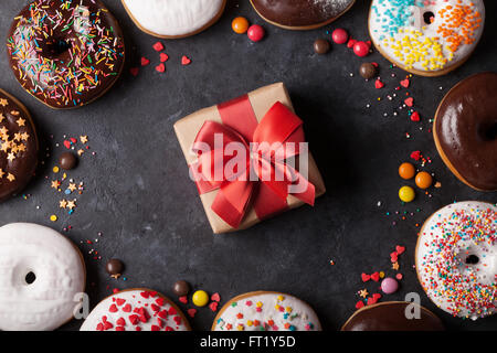 Donuts colorés et boîte-cadeau sur table en pierre. Vue d'en haut Banque D'Images