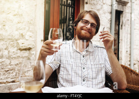 L'Homme barbu beau boire du vin et cigarette assis dans Street Cafe. Banque D'Images