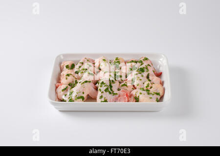 Ailes de poulet crues avec le persil haché dans un plat de cuisson en céramique blanche Banque D'Images