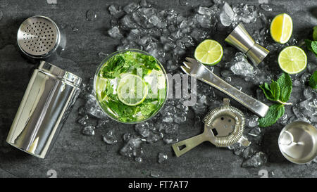 Verre de cocktail avec de la chaux, menthe, glace. Plateau bar tools, shaker, les ingrédients Banque D'Images