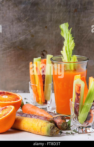 Tranches de carottes et céleri cru coloré comme snack végétarien, d'orange sanguine et le thym avec verre tasse de jus d'orange et de carotte ju Banque D'Images