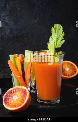 Tranches de carottes et céleri cru coloré comme snack végétarien, d'orange sanguine avec verre tasse de jus d'orange et jus de carotte sur b Banque D'Images