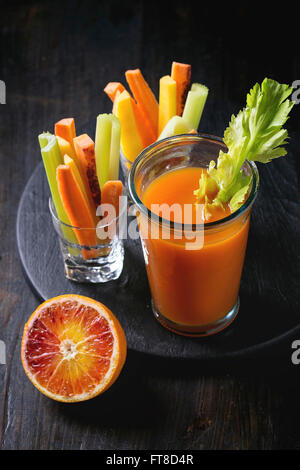 Tranches de carottes et céleri cru coloré comme snack végétarien, d'orange sanguine avec verre tasse de jus d'orange et jus de carotte sur b Banque D'Images