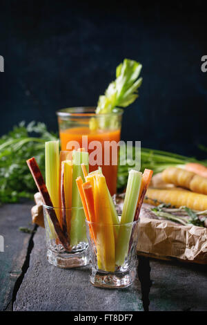 Tranches de carottes et céleri cru coloré comme snack végétarien, et ensemble les carottes avec verre tasse de jus d'orange et jus de carotte ov Banque D'Images