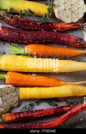 Close up de pelé prêt à cuire les carottes crues colorés avec de l'huile, les herbes de thym frais et de rondelles d'ail dans du bac. Haut de la vie Banque D'Images