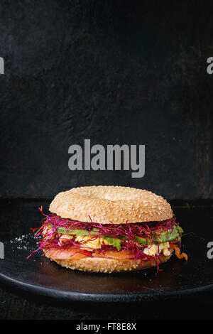 Bagel avec du saumon salé, épinard, betterave germées, d'avocat et œufs brouillés sur planche en bois plus vieux bois dos noir Banque D'Images