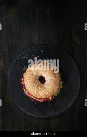 Bagel avec du saumon salé, épinard, betterave germées, d'avocat et œufs brouillés sur planche en bois plus vieux bois dos noir Banque D'Images