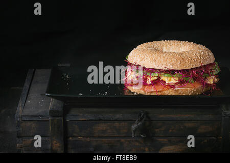 Bagel avec du saumon salé, épinard, betterave germées, d'avocat et oeufs brouillés sur une plaque en céramique noir sur noir Zone de vieux bois Banque D'Images