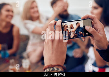 Photographier un groupe d'amis avec téléphone mobile. Les jeunes s'amuser lors d'une fête. Banque D'Images