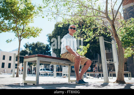 Mature man assis dehors sur un banc et à la voiture. La haute atmosphère homme assis sur une rue de la ville et à la recherche à un Banque D'Images