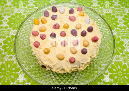 Un gâteau de Pâques ronde décorée de beurre au citron, chocolat mini oeufs sur un vintage glass cake stand Banque D'Images