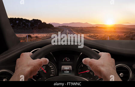 La conduite au coucher du soleil. Vue depuis l'angle du conducteur alors que les mains sur le volant. Banque D'Images