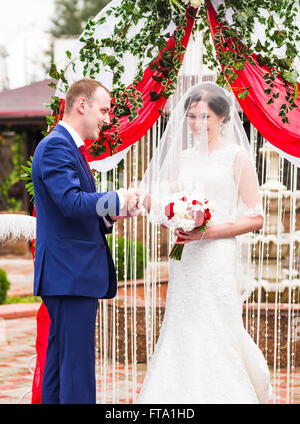 Couple dans une tenue de mariage anneaux change avec arch on background Banque D'Images