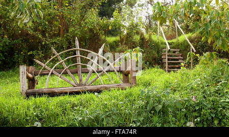 Un banc en bois au design unique se trouve dans une forêt luxuriante avec un escalier en bois menant au loin dans la distance. Banque D'Images