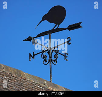 Une grande girouette au sommet d'un garage dans un petit village avec un grand oiseau perché sur la direction du vent l'aiguille contre un ciel bleu Banque D'Images