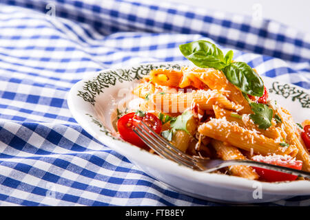 Plaque avec pene pâtes sauce bolognaise tomates cerise haut de persil et les feuilles de basilic sur nappe bleue à carreaux. L'italien et Med Banque D'Images