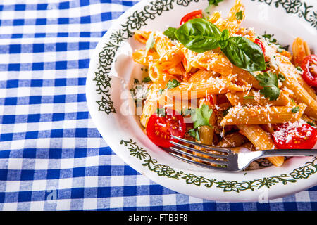 Plaque avec pene pâtes sauce bolognaise tomates cerise haut de persil et les feuilles de basilic sur nappe bleue à carreaux. L'italien et Med Banque D'Images