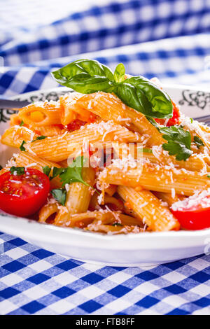 Plaque avec pene pâtes sauce bolognaise tomates cerise haut de persil et les feuilles de basilic sur nappe bleue à carreaux. L'italien et Med Banque D'Images