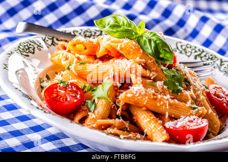 Plaque avec pene pâtes sauce bolognaise tomates cerise haut de persil et les feuilles de basilic sur nappe bleue à carreaux. L'italien et Med Banque D'Images