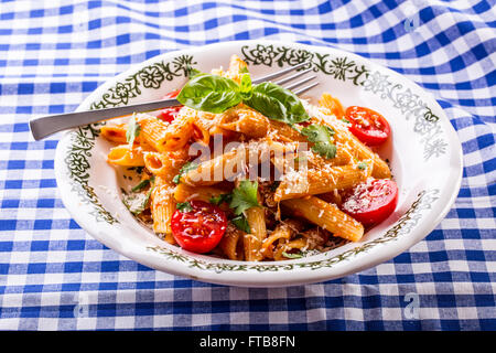 Plaque avec pene pâtes sauce bolognaise tomates cerise haut de persil et les feuilles de basilic sur nappe bleue à carreaux. L'italien et Med Banque D'Images