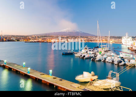 Toits de Catane et son port avec volcan Etna enneigé en arrière-plan après le coucher du soleil Banque D'Images