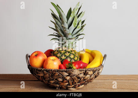 Le panier de fruits avec un ananas, pommes, bananes et fraises à une table en bois Banque D'Images
