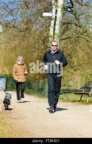 Kristianstad, Suède - 20 mars 2016 : Un homme courir dans le parc en passant une femelle chien avec son chien. Le soleil de l'IRSS Banque D'Images