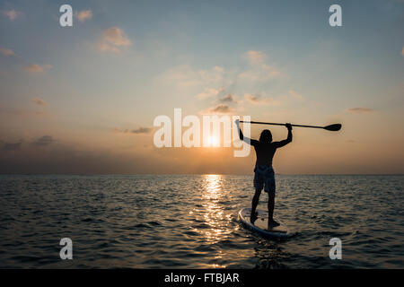 L'homme regardant le coucher du soleil sur un paddleboard, Meeru, Maldives Banque D'Images