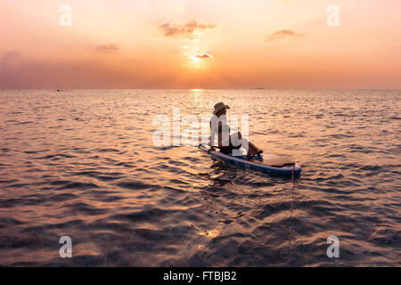 Femme regardant le coucher du soleil sur un paddleboard, Meeru, Maldives Banque D'Images