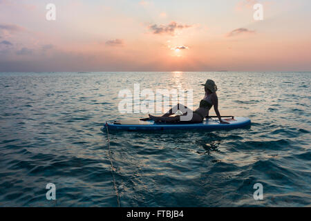 Femme regardant le coucher du soleil sur un paddleboard, Meeru, Maldives Banque D'Images