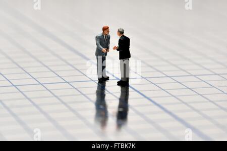 Figurine miniature businessmen having a conversation sur une surface brillante au carré bleu. Banque D'Images