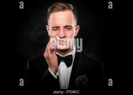 Un jeune homme se sent mal de dents sur fond sombre. Banque D'Images