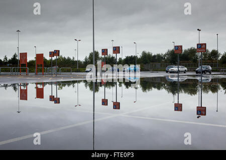 Un parking inondé par forte pluie reflète le ciel et les voitures dans une image miroir du présent abrégé paysage urbain. Banque D'Images