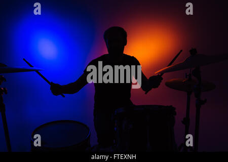 Silhouette of man batteur assis et à jouer de la batterie avec des bâtons sur fond coloré Banque D'Images