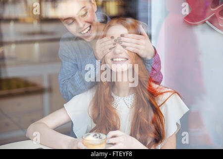 Happy charmante jeune femme ferma les yeux à son amie in cafe Banque D'Images