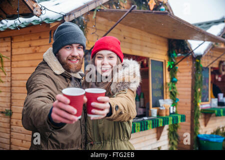 Happy young couple hugging et offrant des boissons chaudes pour vous l'article sur le marché de noel Banque D'Images