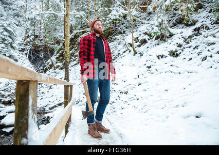 Beau bûcheron barbu en chemise à carreaux holding ax et à la recherche sur les arbres en forêt d'hiver montagne Banque D'Images Beau bûcheron barbu en chemise à carreaux holding ax et à la recherche sur les arbres en forêt d'hiver montagne Banque D'Images