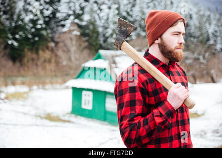 Beau jeune homme en chemise à carreaux et un chapeau avec ax marche dans village Banque D'Images